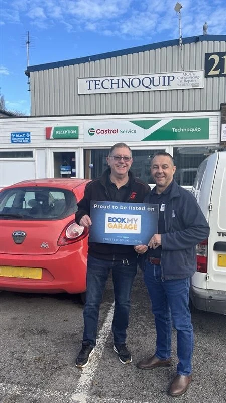 BookMyGarage employee standing outside Technoquip Ltd with garage owner holding BookMyGarage branded card